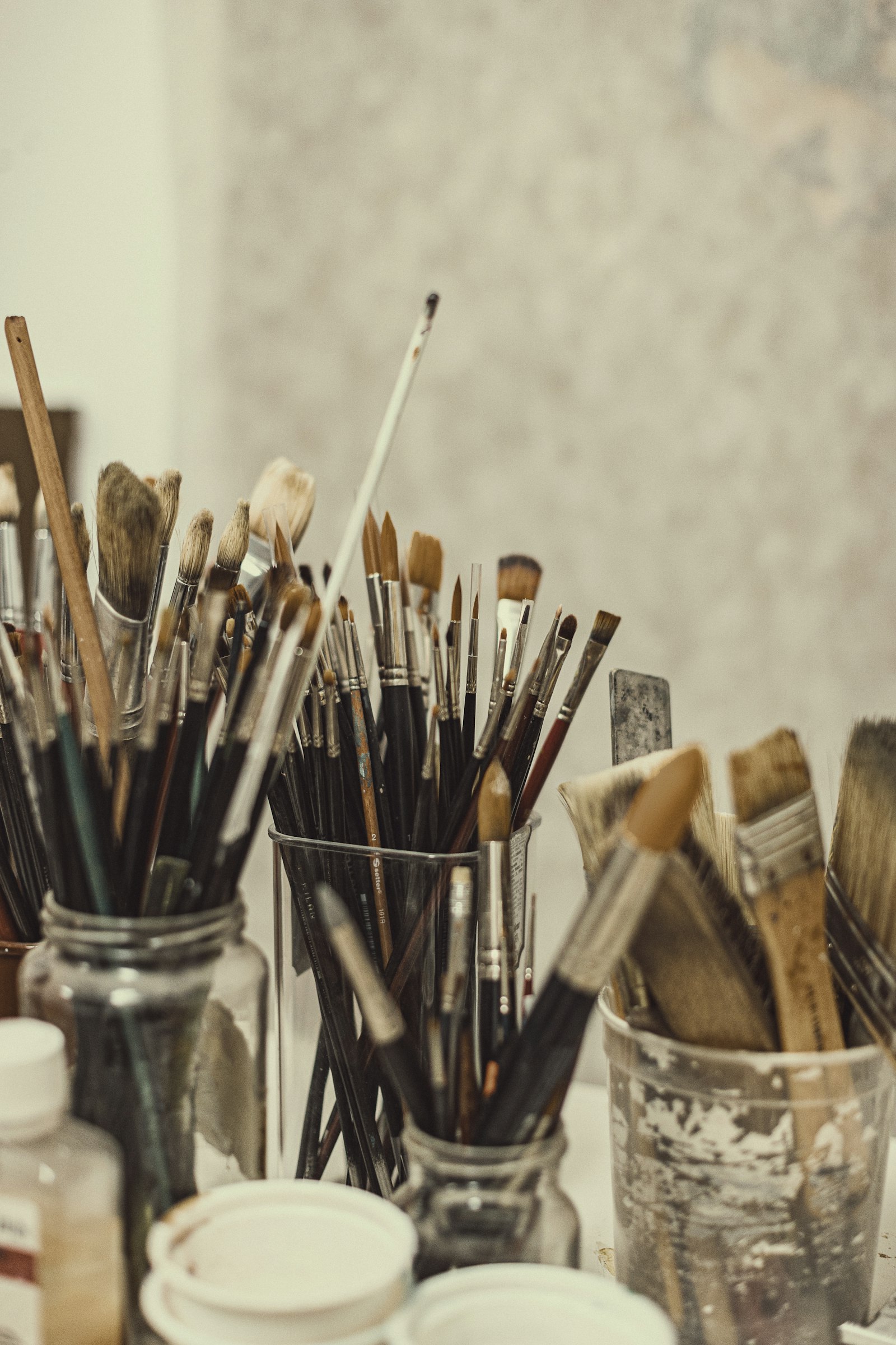 Jars of well-used paintbrushes on an artist's worktable in a light studio (placeholder photo)