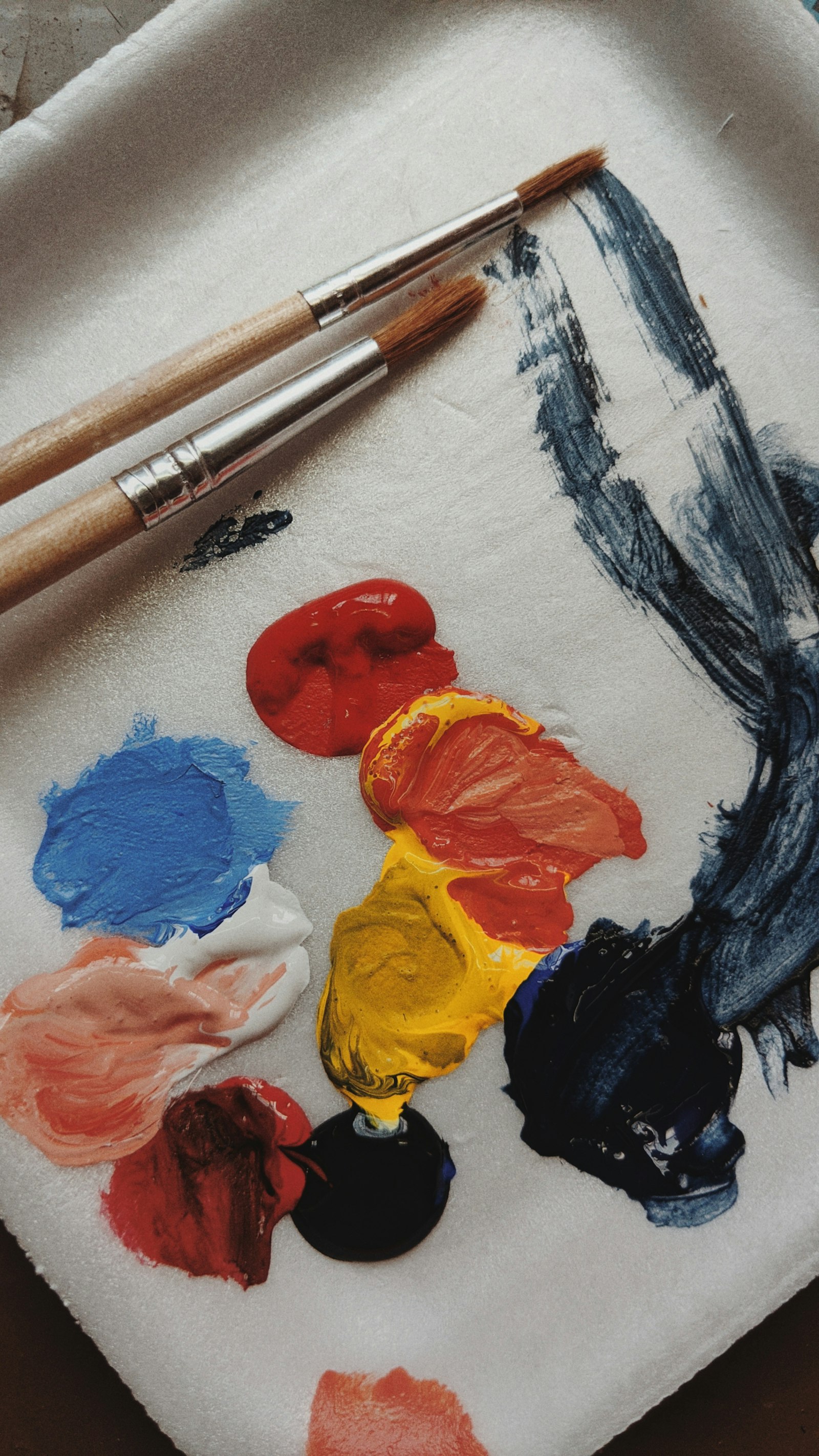 An artist's paint palette streaked with colour, two brushes resting across it (placeholder photo)